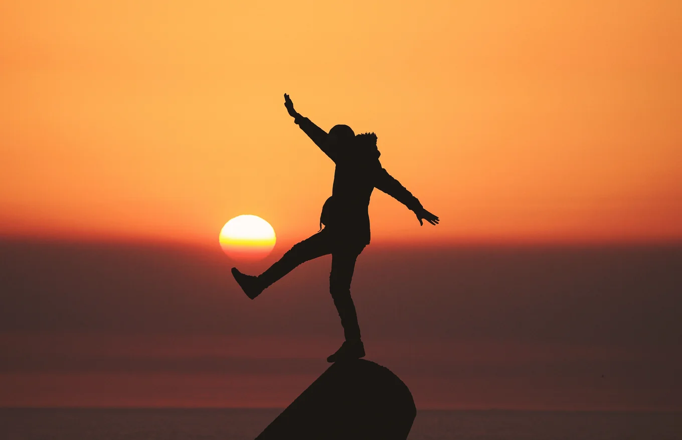 Silhouette of person balancing at sunset.